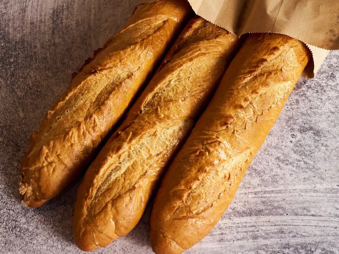 Three fresh baguettes spilling out of a paper bag, baked for Charleston restaurants