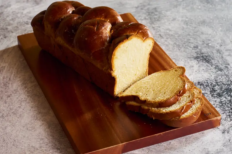 Sliced braided challah loaf on a wooden board
