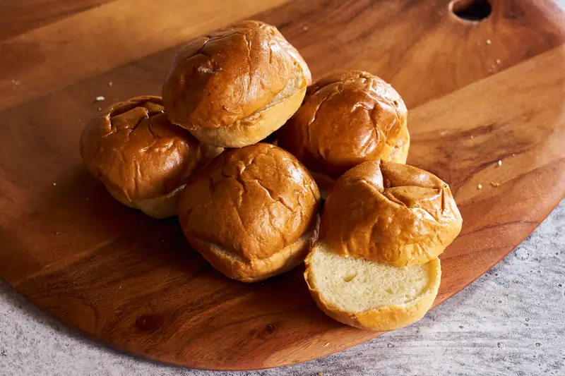 Brioche slider buns on a wooden board, one split open