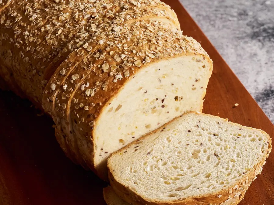 Oat-topped sandwich loaf, sliced on a wooden board